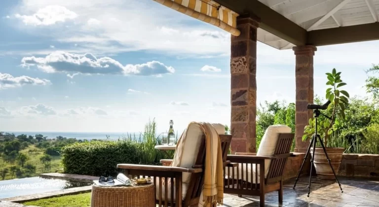 An expansive view from a luxurious safari lodge veranda overlooking a serene landscape, with a calm infinity pool blending into the distant horizon. Near the pool's edge, a pair of sunglasses and a transparent, reusable water bottle filled with fresh water rest on a woven wicker side table, suggesting preparedness for an adventure. Comfortable wooden armchairs with plush cushions invite relaxation, and a high-quality telescope mounted on a tripod promises up-close wildlife sightings, evoking a sense of anticipation for the day's safari explorations. The scene encapsulates a perfect blend of comfort, sustainability, and the thrill of the wild, highlighting the importance of staying hydrated with a reliable water bottle during such excursions.